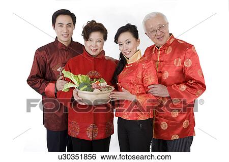 Stock Photograph - Family in traditional clothes holding food to celebrating Chinese New Year and smiling at the camera. Fotosearch