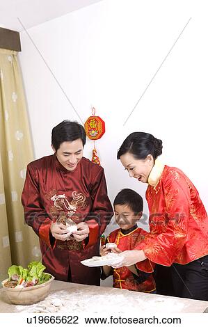 Stock Image - Family in traditional clothes making dumpling together. Fotosearch