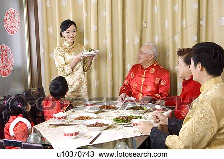 Stock Image - Family members in traditional clothes having dinner together and looking at young woman. Fotosearch