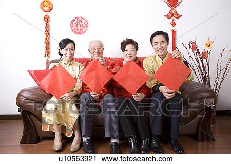 Family members in traditional clothes holding red paper, sitting on the sofa and smiling at the camera View Large Photo Image Stock Image - Family members in traditional clothes holding red paper, sitting on the sofa and smiling at the camera. Fotosearch