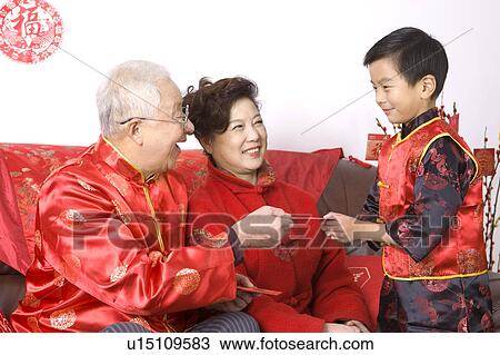 Stock Image - Grandparents in traditional clothes giving red envelope to little boy. Fotosearch