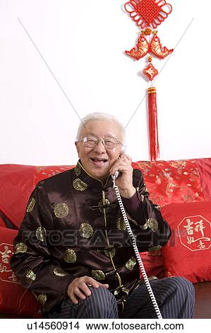 Picture - Senior man in traditional clothes holding the telephone and smiling at the camera. Fotosearch