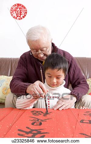 Stock Photograph - Senior man teaching little boy to write Chinese scripts. Fotosearch