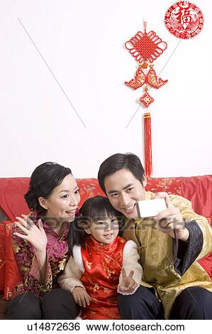 Stock Photograph - Young couple with a child holding a camera and taking picture by themselves. Fotosearch