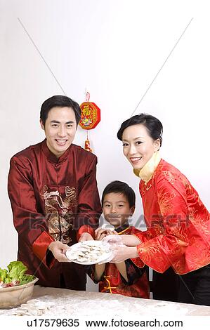 Stock Photography - Young couple with one child making dumpings together and smiling at the camera. Fotosearch