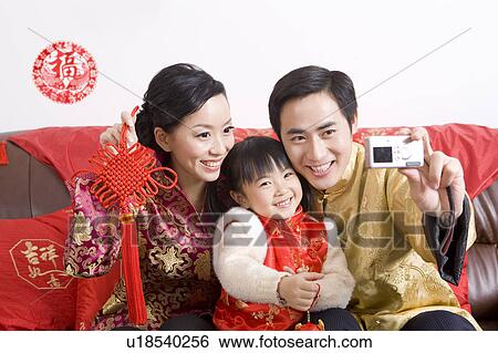 Stock Photograph - Young family with one child in traditional clothes taking photo by themselves and smiling happily. Fotosearch