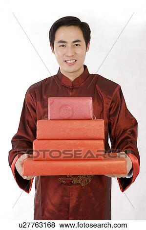 Stock Photo - Young man in traditional clothes holding a stack of gifts and smiling at the camera. Fotosearch