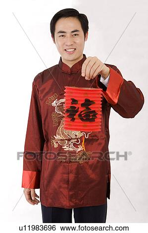 Stock Photograph - Young man in traditional clothes holding Chinese lantern and smiling at the camera. Fotosearch