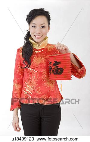 Stock Image - Young woman in traditional clothes holding a Chinese lantern and smiling at the camera. Fotosearch