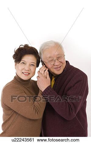 Stock Image - Elderly couple standing together, on the phone. Fotosearch