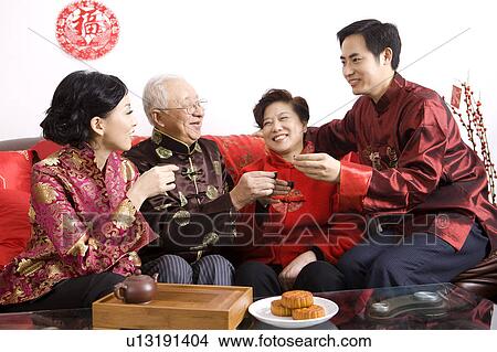Picture - Family members in traditional clothes holding tea cups and smiling happily. Fotosearch