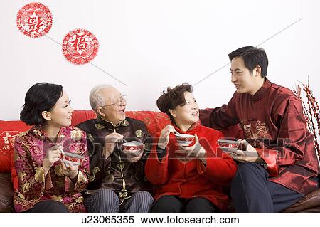 Stock Photography - Family members in traditional clothing holding a bowl and sitting on the sofa. Fotosearch
