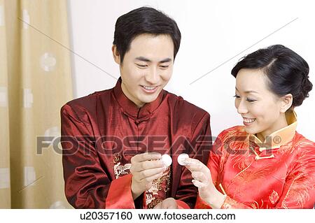 Stock Image - Young couple in traditional clothes holding stuffed dumplings and smiling happily. Fotosearch