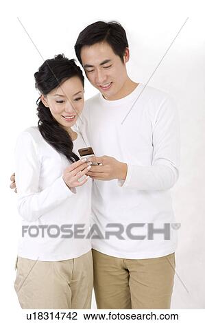 Young couple standing together and looking at the mobile phone, smiling View Large Photo Image Stock Image - Young couple standing together and looking at the mobile phone, smiling. Fotosearch