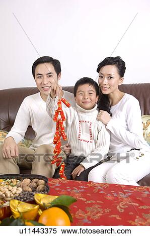 Young couple with one child holding a firecracker decoration, sitting on the sofa and smiling at the camera View Large Photo Image Stock Photography - Young couple with one child holding a firecracker decoration, sitting on the sofa and smiling at the camera. Fotosearch