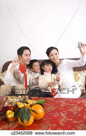 Stock Photo - Young couple with two children sitting on the sofa and taking photos by themselves. Fotosearch