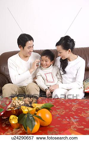 Stock Photo - Young family with one child sitting on the sofa and little boy on the phone. Fotosearch