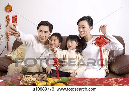 Stock Image - Young family with two children sitting on the sofa, holding tassel and looking away. Fotosearch