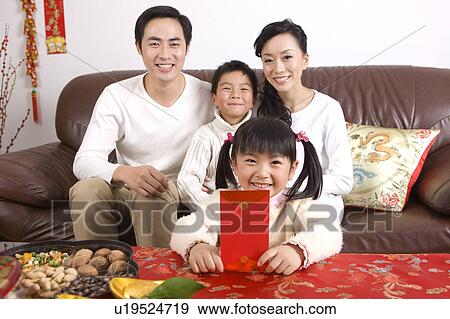 Stock Photo - Young family with two children sitting on the sofa and smiling at the camera. Fotosearch