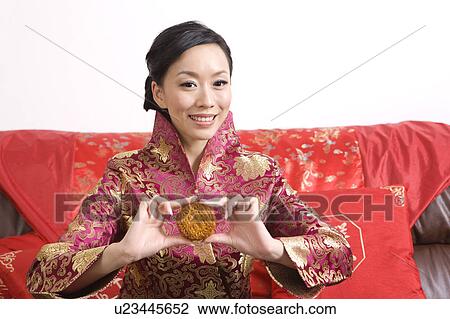 Stock Image - Young woman holding a moon cake and smiling at the camera. Fotosearch