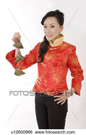 Stock Photograph - Young woman in traditional clothes holding Chinese rice dumpling and smiling at the camera. Fotosearch
