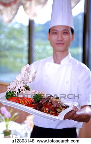 Chef holding a serving dish and looking at the camera View Large Photo Image Stock Photo - Chef holding a serving dish and looking at the camera. Fotosearch