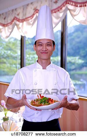 Stock Photo - Chef holding a serving dish and smiling at the camera. Fotosearch