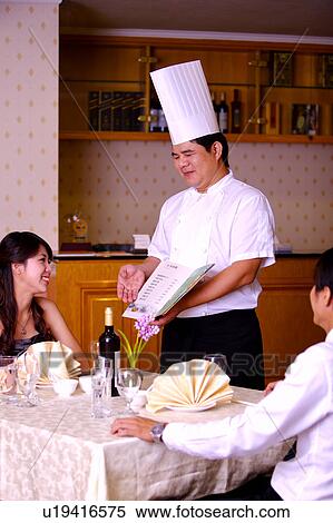 Chef showing the menu to two customers sitting near the table and smiling happily View Large Photo Image Stock Photography - Chef showing the menu to two customers sitting near the table and smiling happily. Fotosearch