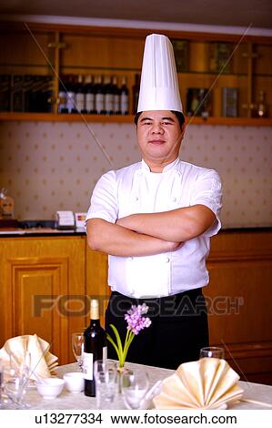 Picture - Chef standing near the dinner table with arms crossed and looking at the camera. Fotosearch