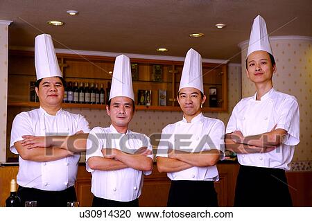 Stock Image - Four chef standing in a row with arms crossed and looking at the camera. Fotosearch
