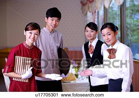 Stock Image - Three waitresses and a waiter gesturing and looking at the camera together. Fotosearch