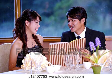 Stock Image - Young man and woman holding the menu and smiling at each other. Fotosearch