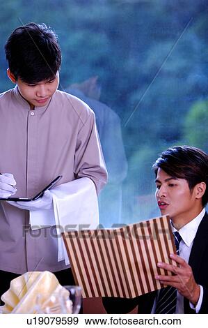 Stock Photo - Young man looking at the menu and telling waiter what he wants. Fotosearch