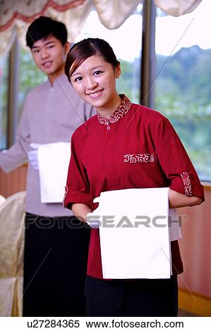 Stock Photography - Young waiter and waitress gesturing and smiling at the camera. Fotosearch