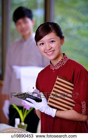 Stock Image - Young waiter and waitress serving and smiling at the camera together. Fotosearch