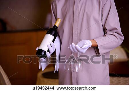 Picture - Young waiter holding a bottle of red wine and wine glasses. Fotosearch