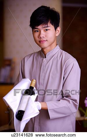 Stock Photo - Young waiter holding a bottle of red wine and looking at the camera. Fotosearch