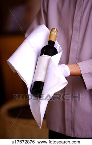 Stock Photograph - Young waiter holding a bottle of red wine with towel around. Fotosearch