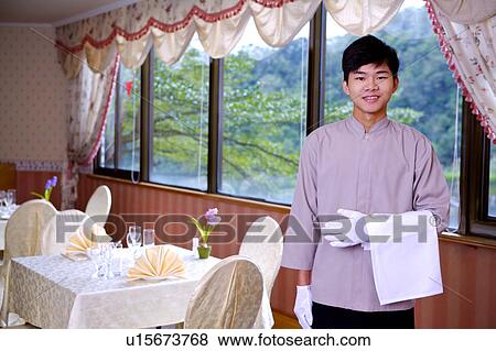 Stock Photo - Young waiter holding a towel and smiling at the camera. Fotosearch