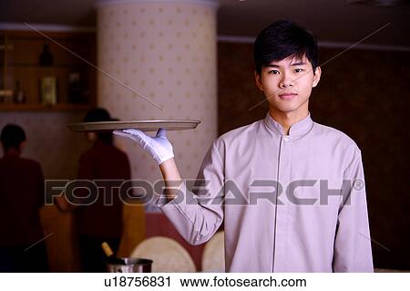 Young waiter holding a tray and looking at the camera View Large Photo Image Stock Image - Young waiter holding a tray and looking at the camera. Fotosearch