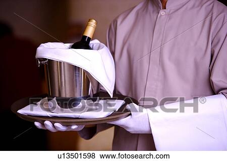 Stock Photo - Young waiter holding a tray with a bottle of red wine. Fotosearch