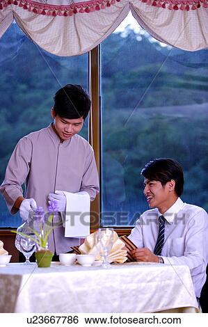 Stock Photograph - Young waiter serving a young customer in a restaurant. Fotosearch