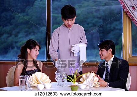Young waiter serving for two customers sitting near the dining table View Large Photo Image Stock Image - Young waiter serving for two customers sitting near the dining table. Fotosearch