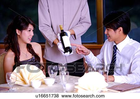 Stock Photo - Young waiter showing a bottle of wine to young man and woman. Fotosearch
