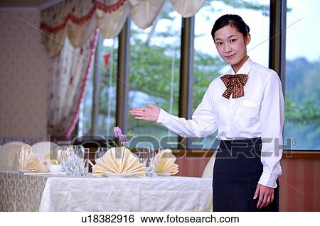Stock Photograph - Young waitress gesturing and looking at the camera. Fotosearch