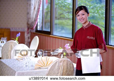 Picture - Young waitress gesturing and smiling at the camera. Fotosearch