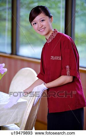 Stock Image - Young waitress gesturing and smiling at the camera. Fotosearch