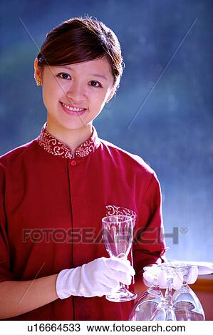 Stock Image - Young waitress holding wine glasses and smiling at the camera. Fotosearch