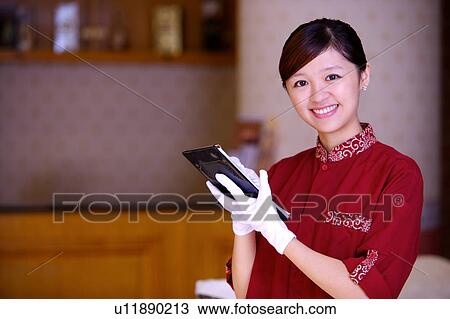 Stock Image - Young waitress writing on the board and smiling at the camera. Fotosearch