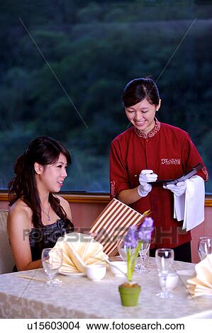 Picture - Young woman holding the menu, young waitress writing on the board. Fotosearch